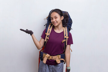 Young asian hiker woman with backpack pointing finger on empty space on white background
