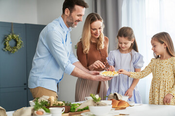 Cheerful caucasian family of four sharing with egg during easter dinner