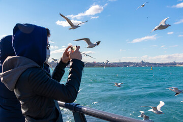 Fototapeta na wymiar Teens with masks taking photograph of seagulls with mobile phones. Back view. Unrecognizable people.