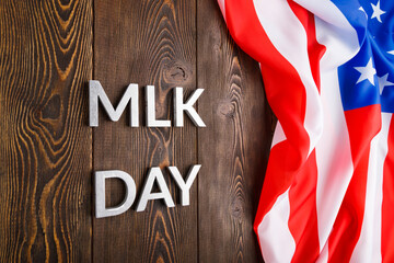 the word MLK day laid with silver metal letters on wooden surface with crumpled USA flag at right...