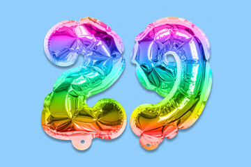 Rainbow foil balloon number, digit twenty nine on a blue background. Birthday greeting card with inscription 29. Top view. Numerical digit. Celebration event, template.