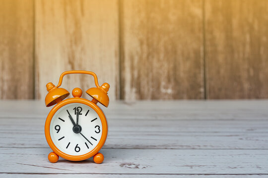 Orange alarm clock isolated on wooden desk. The clock set at 11 o'clock.