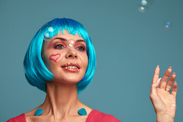 Beautiful young woman with blue wig and bright make-up in soap bubbles. Fashion model girl with...