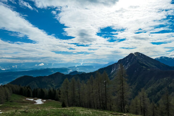 Scenic view on Hahnkogel (Klek) through a dense forest in the Karawanks in Carinthia, Austria. Borders between Austria, Slovenia, Italy. Triglav National Park. Snow capped hills. Woodland, Wanderlust