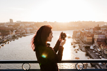 woman in Porto bridge taking pictures with camera at sunset. Tourism in city Europe. travel - obrazy, fototapety, plakaty
