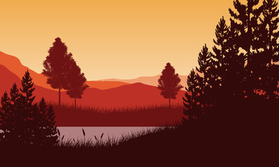 Incredible view of Mountains and lake from the edge of the grass with pine tree silhouettes all around