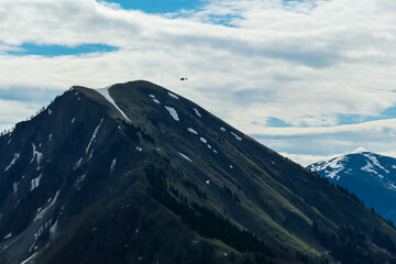 A rescue helicopter flying over the summit of Hahnkogel (Klek) in the Karawanks in Carinthia, Austria. Borders between Austria, Slovenia, Italy. Triglav National Park. Snow capped hills. Woodland