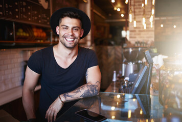 Allow me to satisfy your coffee craving. Shot of a handsome young man working behind the counter of...