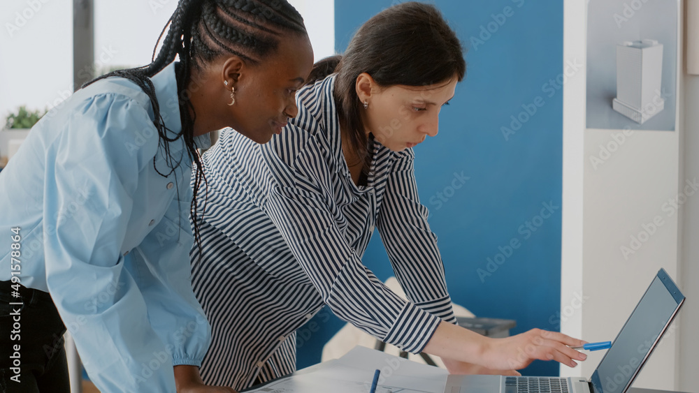 Poster close up of women architects looking at laptop and blueprints plans on table. colleagues using compu