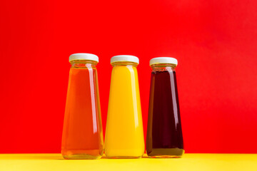 Bottles with yellow and red liquid halthy beverage on yellow and red background. Orange apple cherry
