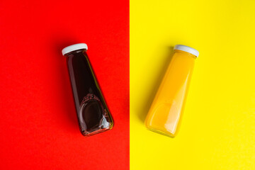 Bottles with yellow and red liquid halthy beverage on yellow and red background. Orange cherry juice