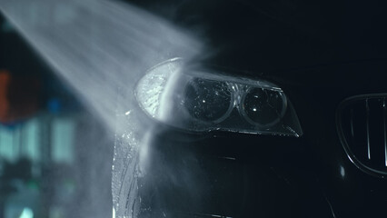 Car headlight wash. Washing modern vehicle body by high pressure jet wash hose water. Auto glass...