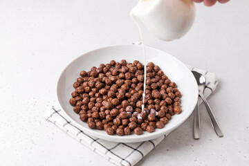 White bowl with chocolate cereal on white table. Served with milk, and spoons. Breakfast and start of the day