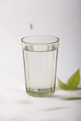Clear glass with water and a light background with plant leaves. Glass of water on white table 