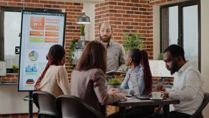 Employee talking to workmates about business presentation, explaining development strategy to audience with analysis charts on monitor. Man uplanning marketing project with coworkers.