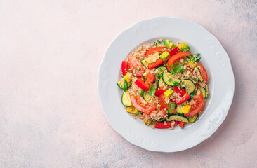 Salad with quinoa and fresh vegetables in a white plate on a light background.