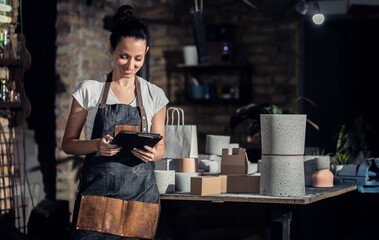 Portrait of craftswoman in apron in her workshop holding tablet.