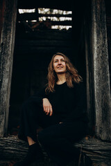 beautiful Ukrainian girl in black clothes near the old wooden house. The war in Ukraine. Portrait of a woman on a dark wooden background. Old abandoned wooden house. Old wooden window frame