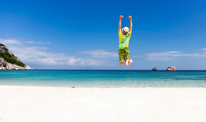 Back view of happy young man jumping with outstretched arms on the beach-Summer vacation concept