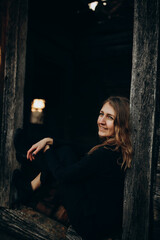 beautiful Ukrainian girl in black clothes near the old wooden house. The war in Ukraine. Portrait of a woman on a dark wooden background. Old abandoned wooden house. Old wooden window frame