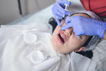 Cosmetologist doing painful lip augmentation procedure with hyaluronic acid. The beautician pierces...