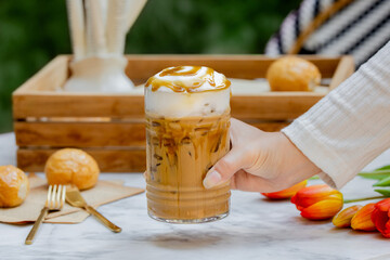 Hand Holding caramel iced coffee glass cup on marble table