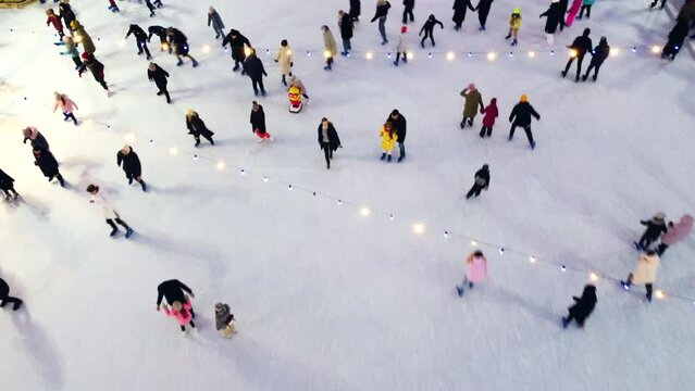 Aerial Drone View Flight Over many people in colorful clothes skating on an open-air ice rink in winter. Ice skating top view. City Park Ice Rink. Winter outdoor activities. Skating sport background