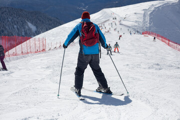 Fototapeta na wymiar A skier rides on a snowy slope. Active rest in the winter. The athlete is preparing for the descent. Mountain ski resort. Outdoor activities on a winter vacation.