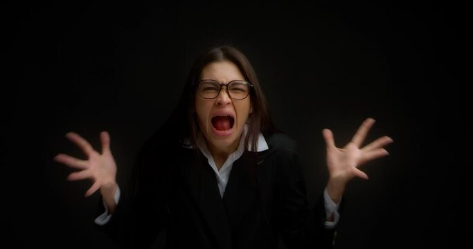 Business woman with glasses, crazy and insane, screaming with an aggressive expression and raised hands. The office manager is tired of work, breaks down and screams with anger on an black background