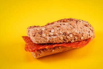 Sandwich with salami and multi-grain bread on a yellow background
