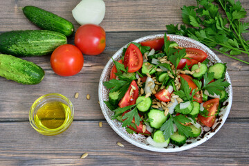 spring salad with tomatoes, cucumber, onion, parsley, seeds and olive oil on rustic background,...