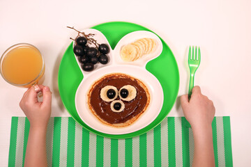 Child ready for breakfast. Fun food for kids. pancakes with berries grape and banana in a rabbit-shaped plate