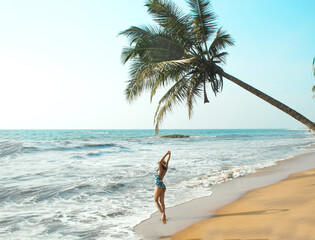  young woman stands under a palm tree on the beach . The concept of vacation and travel to the ocean. Resort on the island. High quality photo