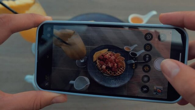 Female hands using smartphone to take photos of tasty waffle with red fruits and mango