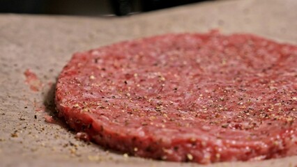 Cook makes meat medallions for burgers. Chef in black food gloves makes cutlet. Cutlets are leveled in steel ring in an even medallion. On top of pouring spices pepper and salt.