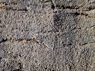 Grayish-brown rough stone surface with some horizontal cracks, texture, wallpaper, background.
