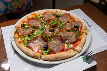 Arugula prosciutto pizza served on white plate