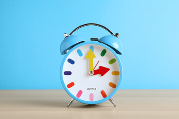 Alarm clock on white wooden table against light blue background