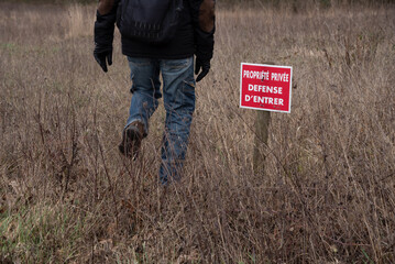 Man does not respect No entry sign for private property (propriété privée défense d'entrer in French) running through private field. France. Violation concept, freedom, right to roam. 