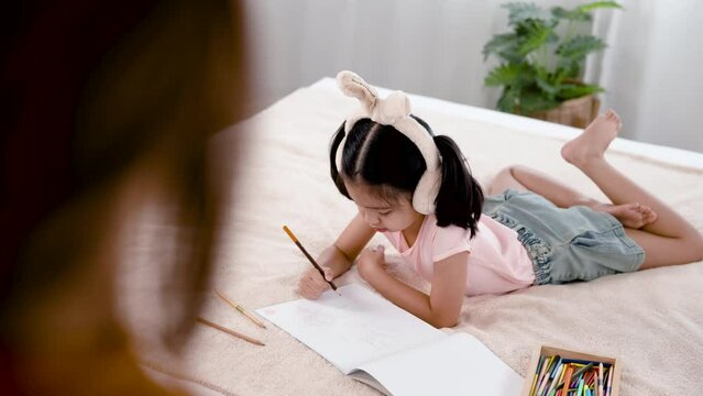 4K 50fps, A adorable Asian girl, tied with both her hair and wearing a bow tie, happily laying on a white bed drawing, her sister stood looking.