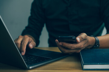 Close up of man hands with mobile phone, Businessman hand using laptop and smart phone working at home office.