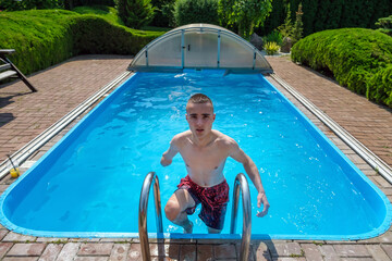 Shirtless male swimmer with amputated arm climbing pool ladder and looking at camera while spending...