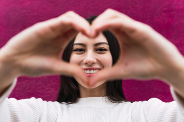 Fototapeta premium Smiling young Asian woman showing shape heart with hands, heart-shape sign looking camera isolated