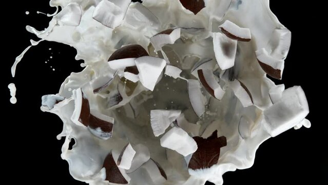Super slow motion shot of rotating exploded coconut cuts and splashing milk on black at 1000fps.