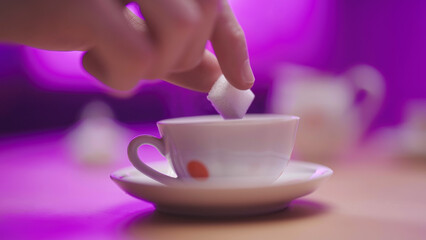 Hand add multiple sugar cube in tea cup close-up