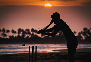 boy playing cricket at sunset on tropical beach in Sri Lanka