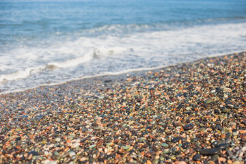 Diagonal coastline of the sea with a pebble beach - colored pebble stones wet from the wave in the foreground and blue water