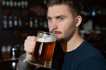 Young man sitting at bar counter with a pint of light beer