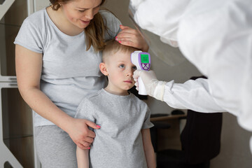 Pediatrician or doctor checks elementary age boy's body temperature using infrared forehead...