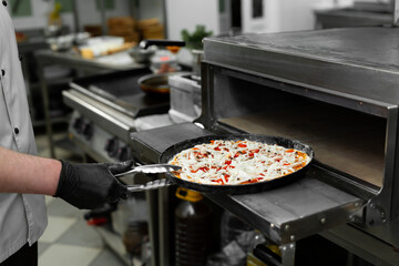 Pizza chef puts pizza in the oven to bake in the oven in the restaurant kitchen